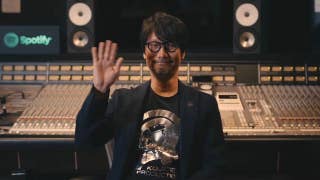 Hideo Kojima sat in front of a mixing desk, waving at the camera with a big grin on his face.