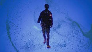 A man, silhouetted, walks towards the screen in a haze of particle effects.