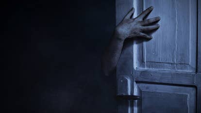 A hand in the dark reaches around an open door, and there's something not quite right about it. A scary image.
