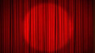 A red stage curtain, drawn, with a circular spotlight shining on the middle of it.