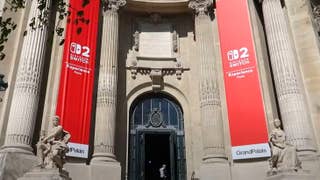 A photograph of the door leading to the Switch 2 reveal event in Paris, in the arched doorway of the Grand Palais. Two large red Nintendo Switch 2 banners hang there. It's hardly subtle.