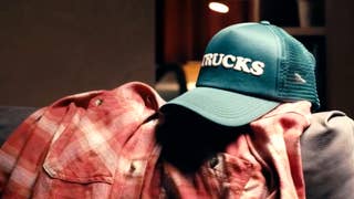 Photo of a green baseball cap with the word "TRUCKS" on it, resting on a red flannel shirt.
